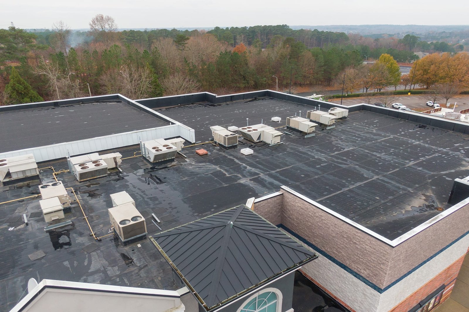 A low-slope commercial roof with rooftop units beside a standing-seam metal roof section